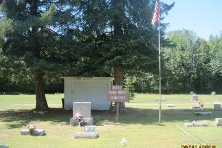 Sunny cemetery scene with American flag and trees.