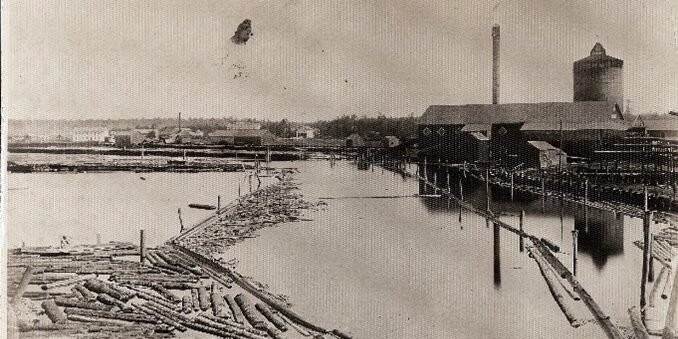 Historical lumber mill with logs in water, vintage industrial scene.